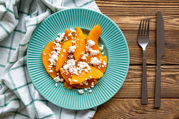 Delicious pumpkin salad on brown rustic table. Brown wooden background, kitchen towel and cutlery.