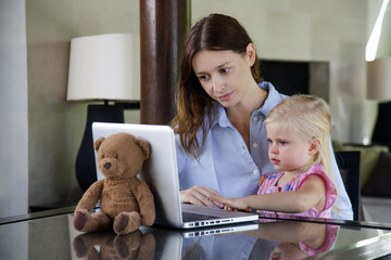 Mother and her little toddler girl sitting in front of laptop. 