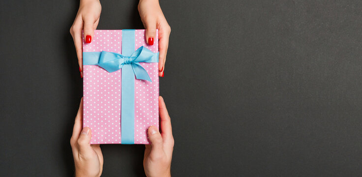 Top View Of Male And Female Hands Holding Present Box On Colorful Background. Sharing A Gift Concept. Copy Space