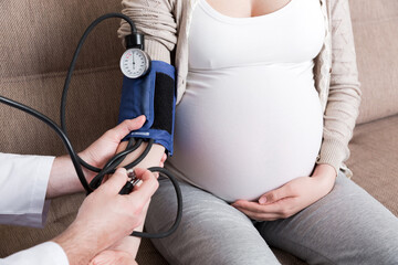 Young doctor is checking blood pressure of pregnant woman at home. High pressure problem during...