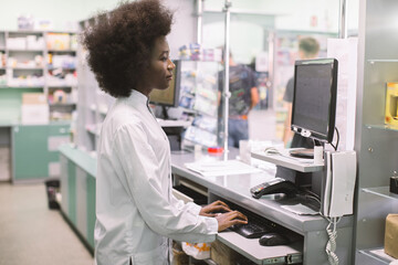 Smiling African American woman clinical pharmacist typing on computer keyboard, while standing...