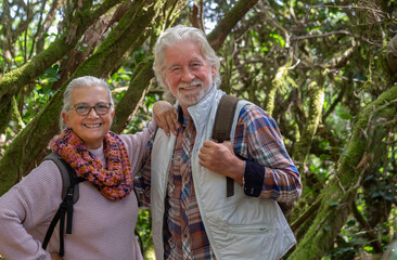 Couple of senior man and woman enjoying mountain hike in the woods among trunks and branches covered with moss during autumn season - concept of fun and active retired seniors