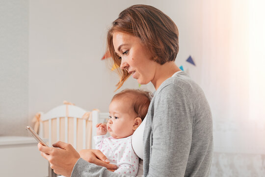 Portrait of a mother holding a baby and using a smartphone. Side view. The concept of motherhood and smartphone use - Powered by Adobe