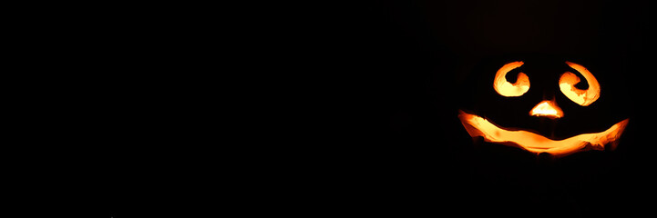 Fototapeta premium glowing smiling face Halloween pumpkin, candle holder, isolated on night dark black background. space for text. banner