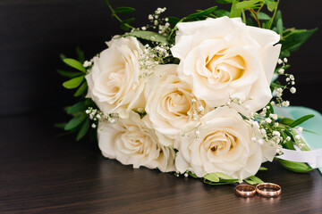 Beautiful bridal bouquet of delicate white roses and gold wedding rings, selective focus