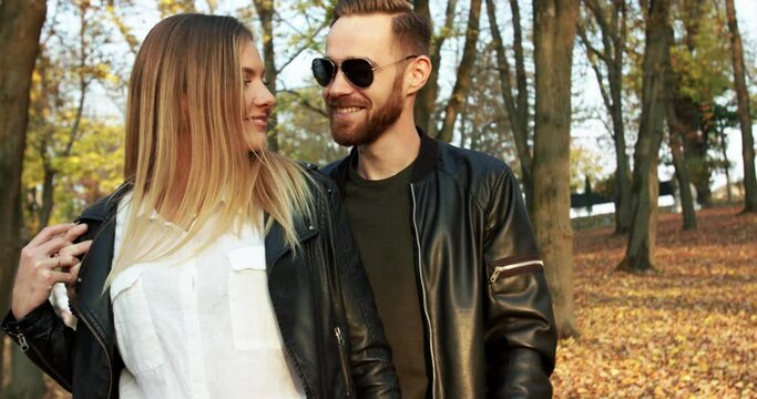 View of brutal man in sunglasses kisses his happy girl in autumn park