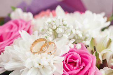Gold wedding rings on a bouquet of white and pink flowers, selective focus