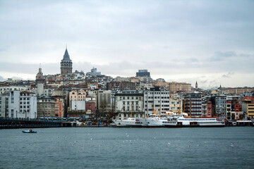 Fototapeta premium Galata Tower, on its hill, in Karakoy and Beyoglu district, taken during a cloudy winter afternoon, while the sea, ferry boats and cargo ships can be visible in foreground in Istanbul, Turkey