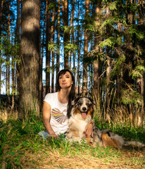 Young brunette woman sitting in nature in the woods with an Australian shepherd dog