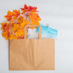 Maple leaves, a paper bag and a medical mask. On white background. View from above . There is room for text. Autumn layout. Horizontally