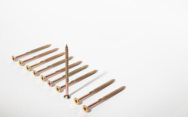 Construction metal screws of gold color on a white background lie in a row, and one stands. Self-tapping screws as a background. Place for text