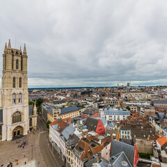 Obraz premium Facade of St Bavo Cathedral with its imposing tower in an aerial view, cityscape with houses and buildings in the center of Ghent city, cloudy day with a cloud covered sky in Belgium
