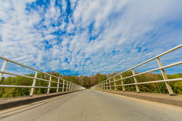 Elsloo Bridge with its white metal railing with a deep perspective on the Juliana canal with lush trees in the background, sunny day with a blue sky and white clouds in South Limburg, Netherlands