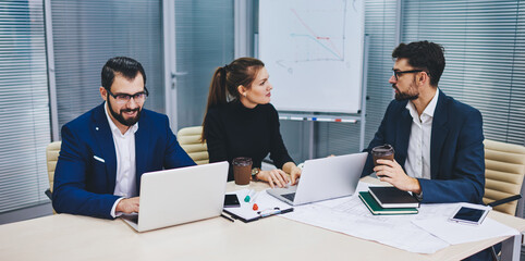 Male and female professional entrepreneurs analyzing information from website on laptop computer during collaboration briefing, group of confident employees sitting at office desk and talking
