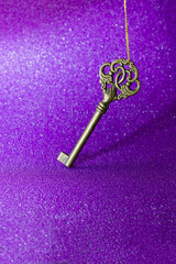 Old door key on purple glitter cardboard. The concept of security, finding a solution or discovering a secret. Selective focus, vertical orientation.