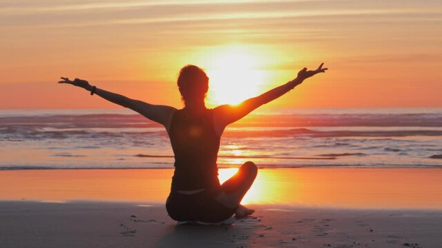 Silhouette of slim woman with arms raised up on the beach at sunset