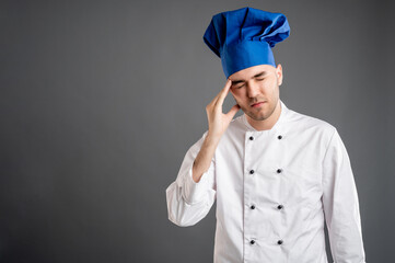 Young male dressed in a white chef suit has headache