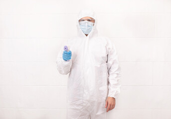 Male practitioner in protective medical costume and surgical mask standing with infrared thermometer for temperature measurement during coronavirus epidemic.