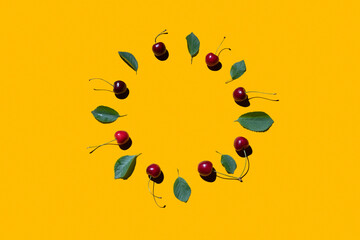 Ripe red cherry fruits on yellow background laid out in a circle