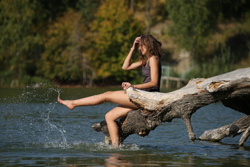 Fototapeta na wymiar a girl sitting on a snag and sprinkling water with her foot