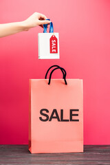 cropped view of woman holding small shopping bag with sale tag near paper package on pink, black...