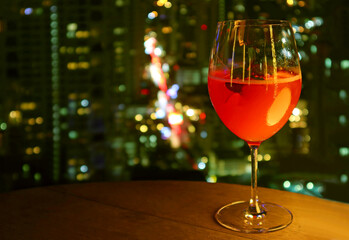 Glass of vivid red cocktail isolated on the rooftop terrace's table with blurry urban night view in background