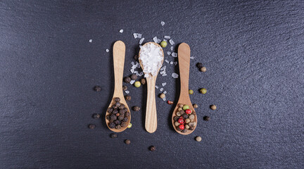 Salt and whole black peppercorns, pepper mix in wooden spoons, top view