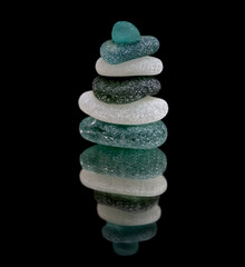 small sea glass pyramid isolated on black, reflective surface