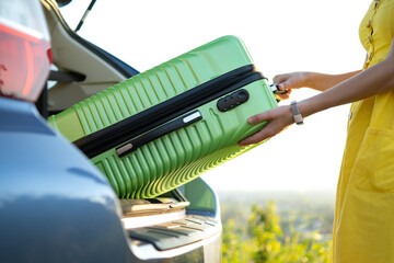 Close up of woman hands taking green suitcase from car trunk. Travel and vacations concept.