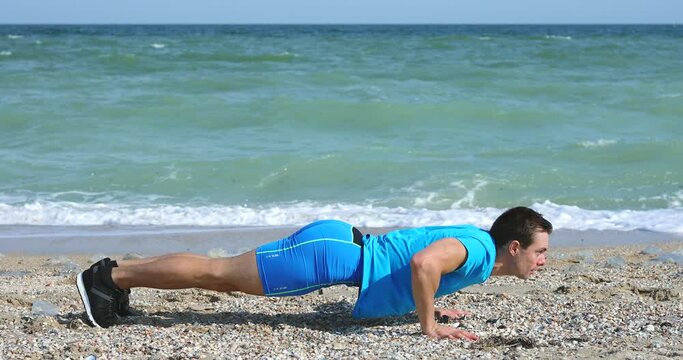 Young man doing push-ups at beach working out exercise with ocean background