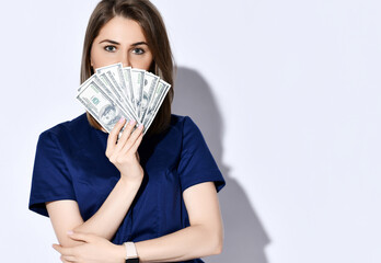 Portrait of young beautiful woman dentist, doctor, nurse holding fan of dollars cash bills in front of her face