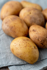 Raw unpeeled potato on light wooden kitchen table with cotton cloth aside, close up, catalogue photo