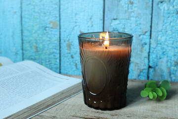 nice aromatic scented glass candles are displayed on the wooden table with a book and background of blue wooden strip wall outside the house which the color peeling off 