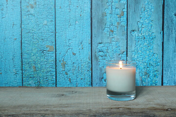 nice aromatic scented glass candles are displayed on the wooden table with a book and background of blue wooden strip wall outside the house which the color peeling off 