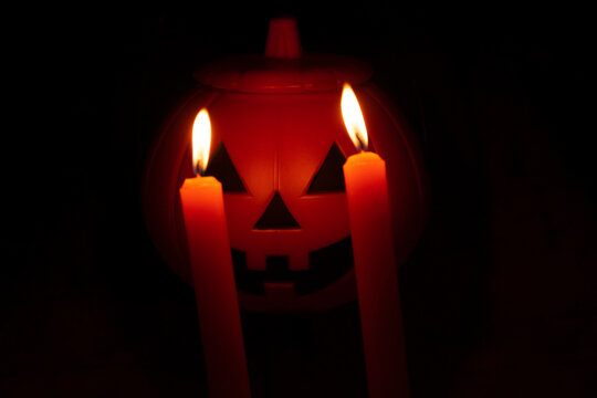 Halloween theme. orange Candles with fire like the eyes of a terrorific pumpkin on black background