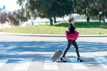 Side view of the cheerful business woman carrying the luggage while holding a red shoulder bag