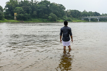 Young Indian man bathing in fresh water river Periyar Kerala India. calm refreshing lake. Lush green vegetation and flowing river.