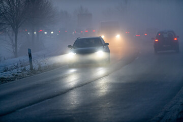 Luminous car headlights in the twilight in fog.