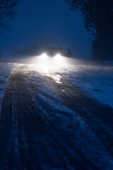 Naklejka premium Luminous car headlights in the night in fog on snow track.