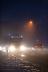 Fototapeta na wymiar Luminous car and truck headlights in the night in fog on winter street.