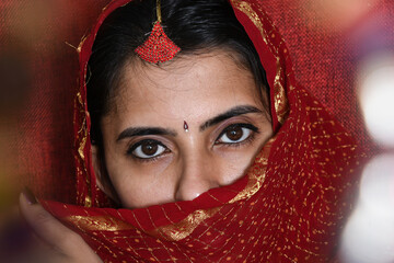 Close up of beautiful Indian girl eyes . Young hindu woman model with  kundan jewelry . Traditional Indian costume red saree or sari . Indian or Muslim woman covers her face.