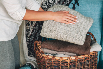 Women's hands fold a stack of warm knitted sweaters in  wicker basket 