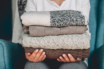 Female hands hold a stack of warm knitted sweaters