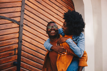 Obraz premium Young adorable happy hipster african american couple having piggyback ride while walking on the street in an old city.