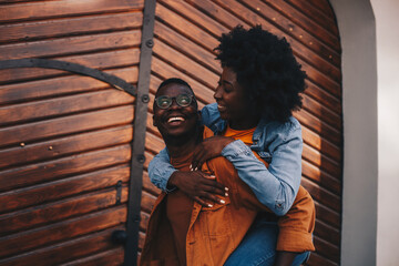 Young adorable happy hipster african american couple having piggyback ride while walking on the street in an old city.