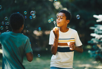 Cute african boy blowing bubbles outdoors with his friend and having fun on beautiful sunny day.