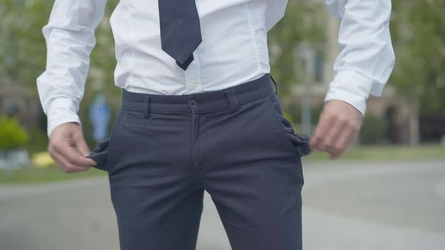 Unrecognizable bankrupt businessman showing empty pockets outdoors. Insolvent Caucasian man having no money. Unemployed office worker standing on city street.