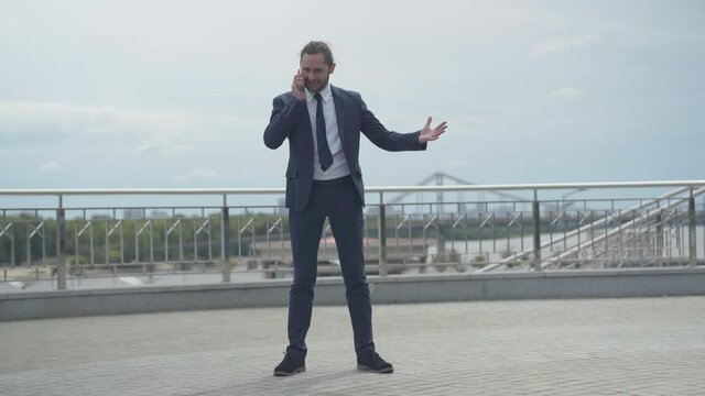 Wide shot of businessman yelling on phone freaking out. Portrait of angry young Caucasian male CEO shouting and gesturing outdoors in urban city. Business problems concept.