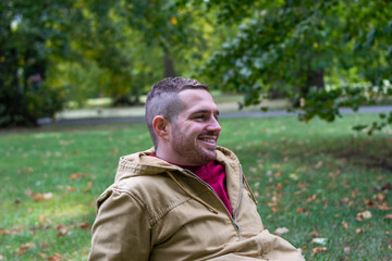 Photo of a young and attractive man sitting on the park smiling and enjoying a sunny day