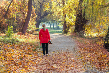 A girl in a red jacket walks barefoot along a path in an autumn park